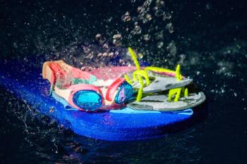 Schwimmbrille und Tauchringe auf einem Schwimmbrett im Wasser mit spritzenden Wassertropfen.
